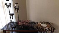 Photo showing three metal and glass candlesticks with crystal droplet accents, faux flowers, metal basket, and starburst mirror laid on black surface.