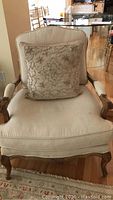 Front view of beige upholstered chair with wooden frame and decorative pillow on seat.