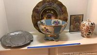 Group shot of the metal platter, hand painted bowl with gold trim and blue accents, Asian art piece in Lucite display, and ginger jar.