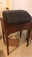Black plastic carrying case closed on top of a wooden sewing machine table.