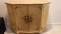 Full front view of hand painted wooden cabinet showing floral designs and two middle doors with round knobs.