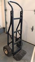 Side view of black metal Harper hand truck with curved handle and pneumatic tires showing full frame and loading plate.
