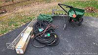 Photo of all items in the lot placed on driveway, including metal rack shelf, garden hoses, grass seed spreader, and boxed mulching kit