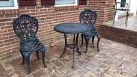 Full view of rolled steel garden table with two matching small decorative metal chairs on outdoor patio