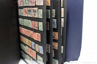 Photo showing close-up of multiple pages of vintage stamps mounted in black album pages inside a blue binder.