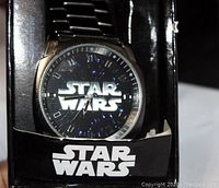 Star Wars wristwatch with black dial showing 'Star Wars' logo and stainless steel band in original black branded box.