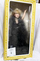 Frontal view of the Effanbee Mae West doll inside its original yellow and white box, showing the doll fully with a black feather boa and blonde curls.