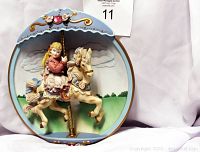 Front view of the 3D musical carousel decorative plate showing a girl riding a carousel horse with decorative blue background and gold accents.