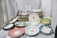 Over 40 assorted vintage fine china plates of various sizes and patterns displayed on white drape.