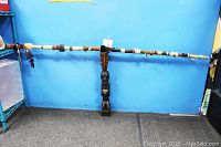Full view of the entire lot against a blue background showing the tall carved wood statue and the long decorated walking stick with leather, beads, and feathers.