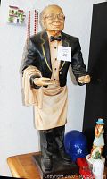 Full view of vintage butler statue standing on a wooden surface showing attire and condition.