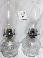 Two clear glass oil lamps with metal wick holders and etched rose designs on the bases, shown against a white backdrop with a MaxSold label.