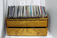 Wooden CD storage box with built-in drawer and 30 assorted CDs placed on top, angled to show drawer and CD slots.