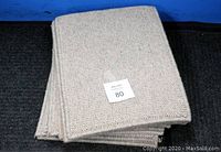 Stack of beige wool woven carpet door mats showing texture and edges.