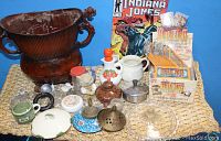 Wide shot showing all items in the lot including large brown planter, various pottery lids, and trading card display box with comic book behind