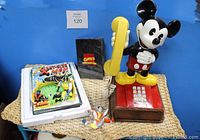 Full view of Marvel Comic Cover Sculpture with X-Men characters and certificate of authenticity plus vintage Disney Mickey Mouse telephone on woven surface against blue background.