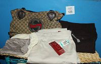 Photo showing two pairs of folded slacks and the Gucci purse resting on a wicker surface against a blue wall.