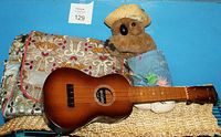 Full view of a vintage-style ukulele, a patterned backpack, and a plush koala bear clip arranged together.