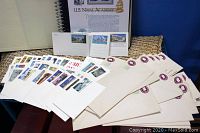 Selection of stamped postcards and envelopes arranged in front of an informational binder about U.S. Naval Academy commemorative stamps