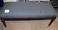 Top and side view of the grey fabric and wood dressing bench on a tiled floor, showing fabric surface condition and wooden legs.