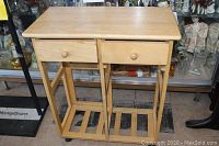 Front view of light wood microwave cart showing two drawers and open slatted shelving below.