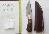Damascus steel straight knife with wood handle and mosaic pins alongside brown leather sheath and measuring tape