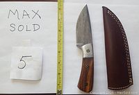 The Damascus straight knife with wood handle, mosaic pins, and leather sheath is displayed next to a measuring tape showing approximate length.