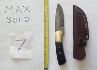 Image of Damascus straight knife alongside brown leather sheath and measuring tape showing blade length.