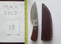 Photo showing Damascus straight knife with polished buffalo horn handle and brown leather sheath with white stitching.