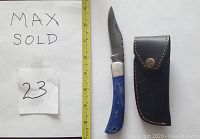 Photo of Damascus folding knife with dyed blue bone handle next to a ruler for scale and black leather sheath.