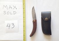 Folding Damascus knife with wood handle next to measuring tape and leather sheath to show size and details.
