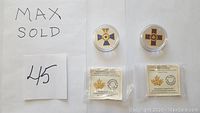 Two coins showing obverse sides with colored crosses, plus two certificate of authenticity pouches