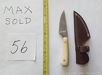 Photo showing the Damascus straight knife with cream-colored camel bone handle and brown leather sheath beside a ruler for scale.