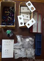 Overview of lot showing cardboard boxes filled with coin flips, plastic capsules in bags, storage boxes, and some water bottle holders.