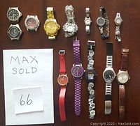 Top view showing entire lot of 12 watches on wooden surface, various styles and colors, with Max Sold paper label.