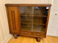 Full front view showing sliding tempered glass doors, side wooden door and two wooden drawers beneath with carved handles.