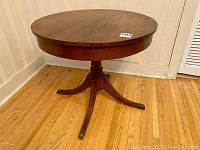 Full view of round walnut occasional table showing top and pedestal base with four splayed legs ending in metal caps.