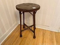 View of the antique wicker plant stand from an angle showing three legs and braided edge on the top.