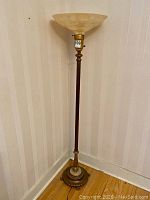 Full view of the tall antique Art Deco torchiere floor lamp showing wooden shaft, ornate base with metal and marble accents, and cream colored pressed glass shade.