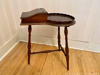 Side view showing slender turned legs and lift-top compartment with scalloped tray surface