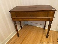 Front angle view of antique solid wood desk with fold-down lid closed and turned legs.