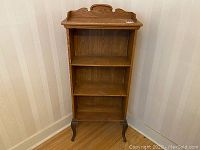 Front view of the small antique ash wood bookcase with cast metal legs on wooden floor against wall