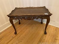 Antique carved wood coffee table showing front and side with scalloped carved edges, cabriole legs, and claw feet.