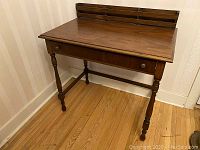 Front and left side view of antique walnut desk showing turned legs, stretcher supports, single drawer with brass knob, and medium brown finish.