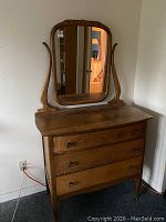 Photo showing the full antique solid ash 3 drawer dresser with attached vanity mirror, displaying curved wood framing and round metal drawer handles.