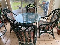 Full view of the vintage green painted rattan table with round glass top surrounded by four matching chairs with floral cushions.