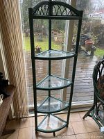 Full view of the vintage rattan corner shelf with four glass shelves placed near a window showing its shape and design.