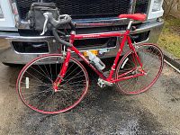 Full view of red Jamis Ventura Sport road bicycle with drop handlebars, water bottle, cage and handlebar bag