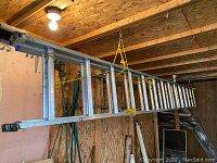 Side view of the full 28-foot aluminium extension ladder hanging horizontally by yellow ropes inside a wooden shed.