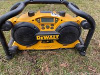 Front view of yellow and black DeWalt DC011 work site radio with speakers, control buttons, digital display and protective metal frame.